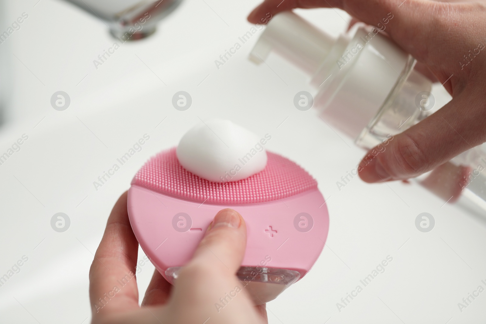 Photo of Washing face. Woman applying cleansing foam onto brush above sink in bathroom, closeup