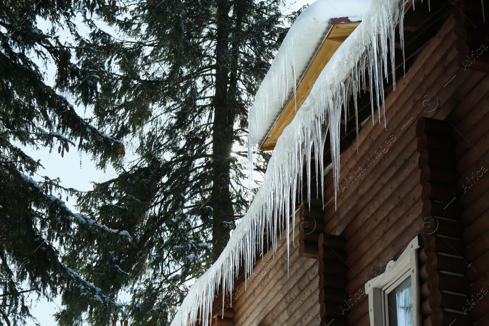 Photo of House with icicles on roof, low angle view. Winter season