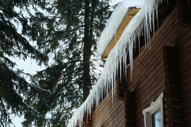 House with icicles on roof, low angle view. Winter season