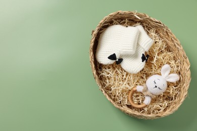 Photo of Different baby accessories in wicker box on green background, top view. Space for text