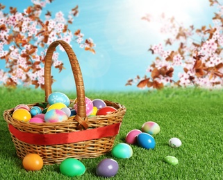 Image of Wicker basket with Easter eggs on green grass outdoors, space for text