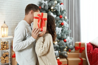 Couple kissing while hiding behind Christmas gift at home