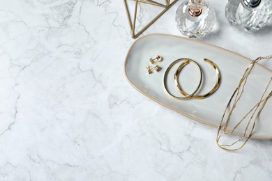 Photo of Different elegant bijouterie and bottles of perfume on white marble table, flat lay. Space for text