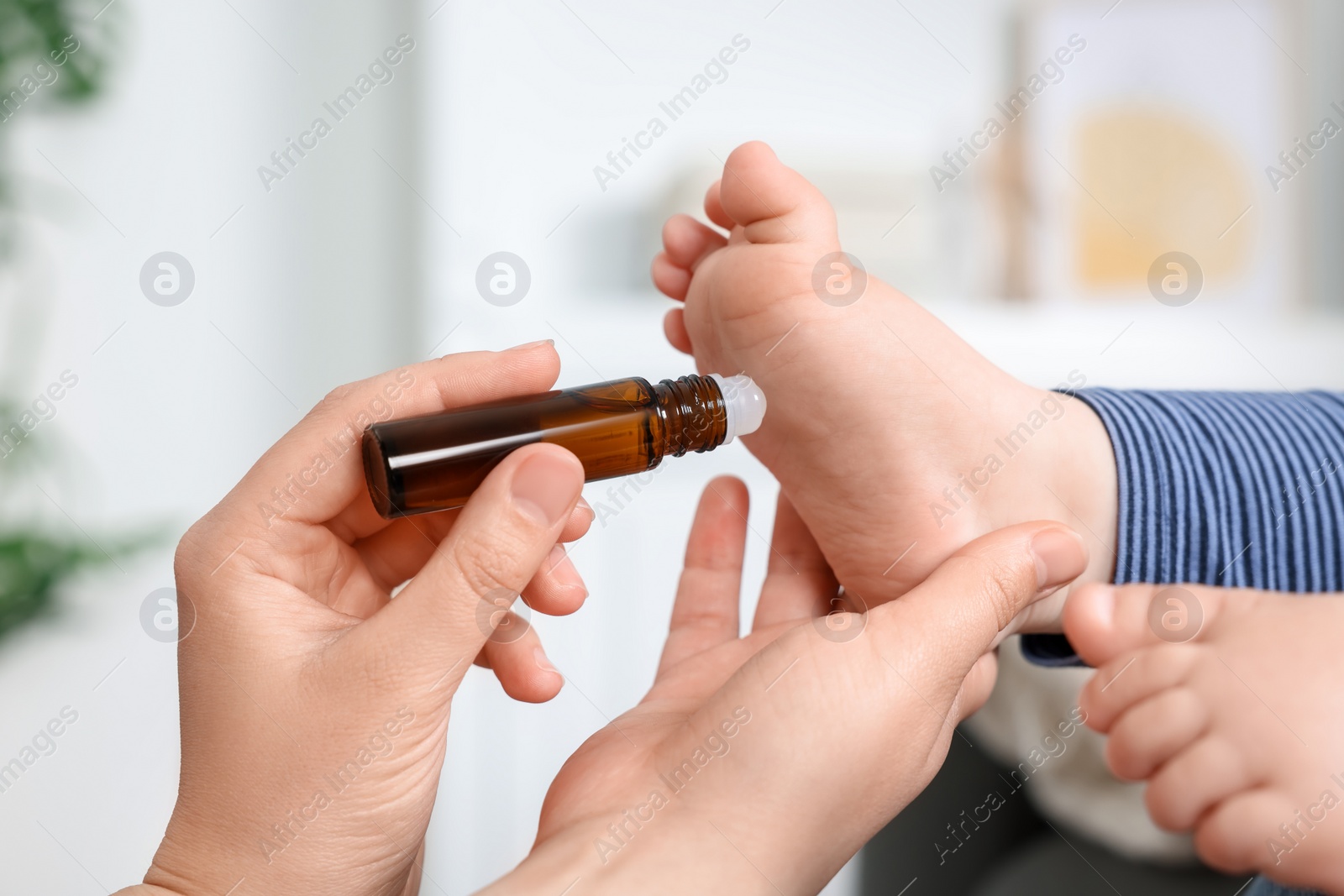 Photo of Mother applying essential oil from roller bottle onto her baby`s heel on blurred background, closeup