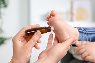 Mother applying essential oil from roller bottle onto her baby`s heel on blurred background, closeup