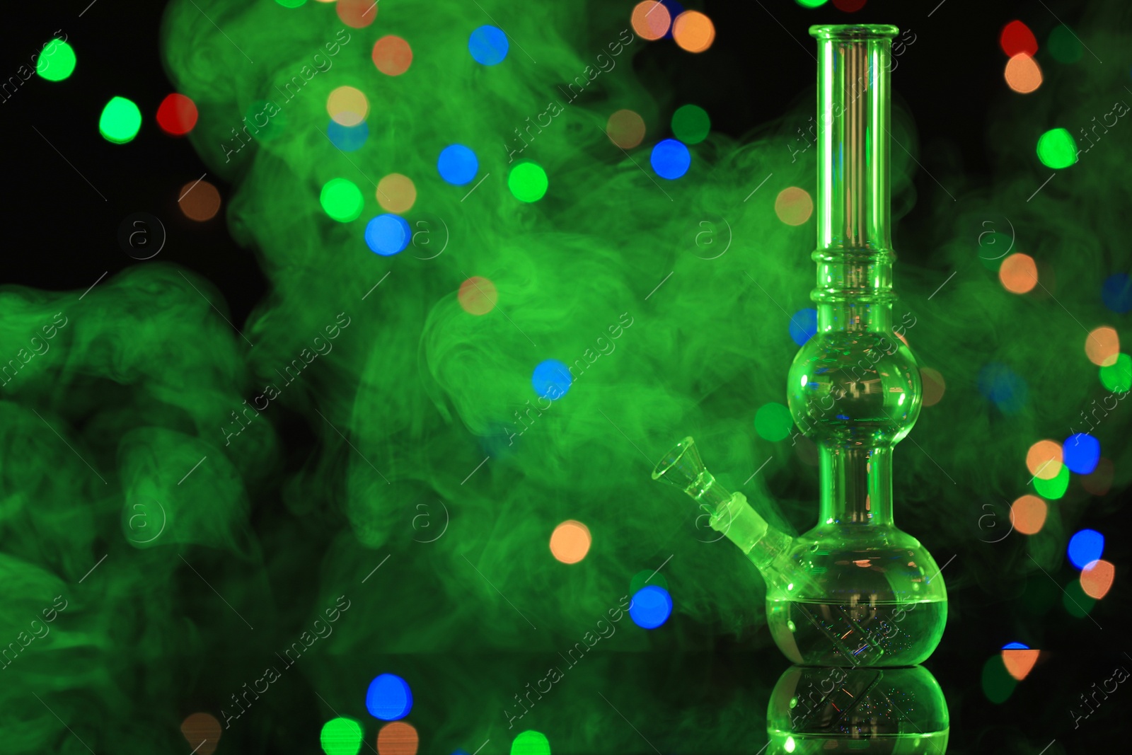 Photo of Glass bong with smoke against blurred lights, space for text. Smoking device