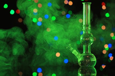 Photo of Glass bong with smoke against blurred lights, space for text. Smoking device