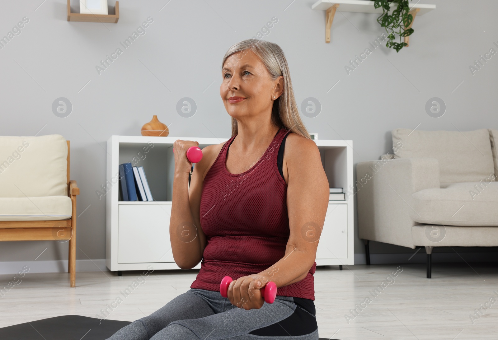 Photo of Senior woman exercising with dumbbells at home. Sports equipment