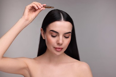 Photo of Beautiful young woman using ampoule for hair treatment on grey background