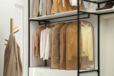 Photo of Garment bags with clothes on rack in dressing room