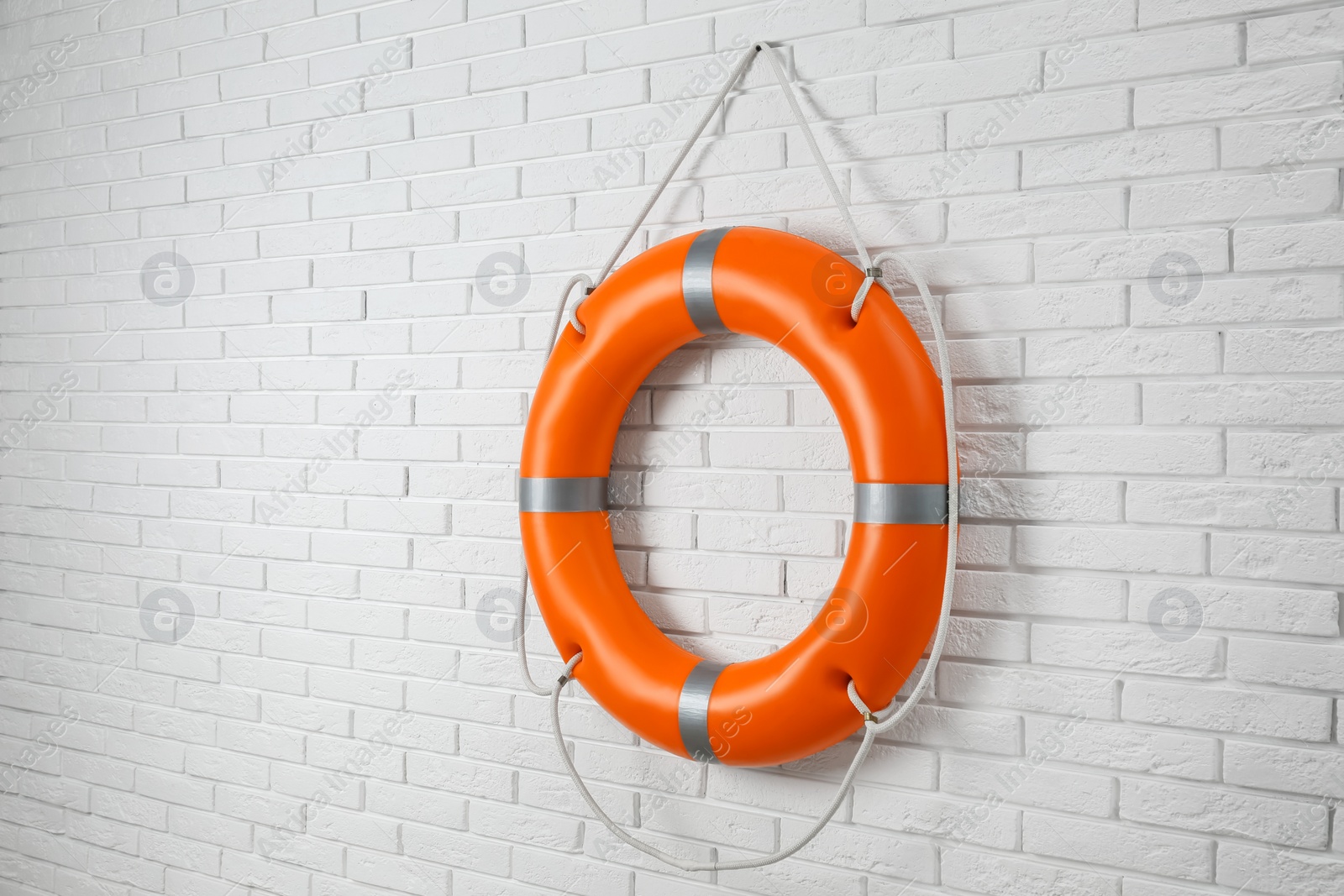 Photo of Orange lifebuoy and space for text on white brick wall. Rescue equipment