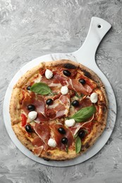 Photo of Tasty pizza with cured ham, olives, sun-dried tomato and basil on gray textured table, top view