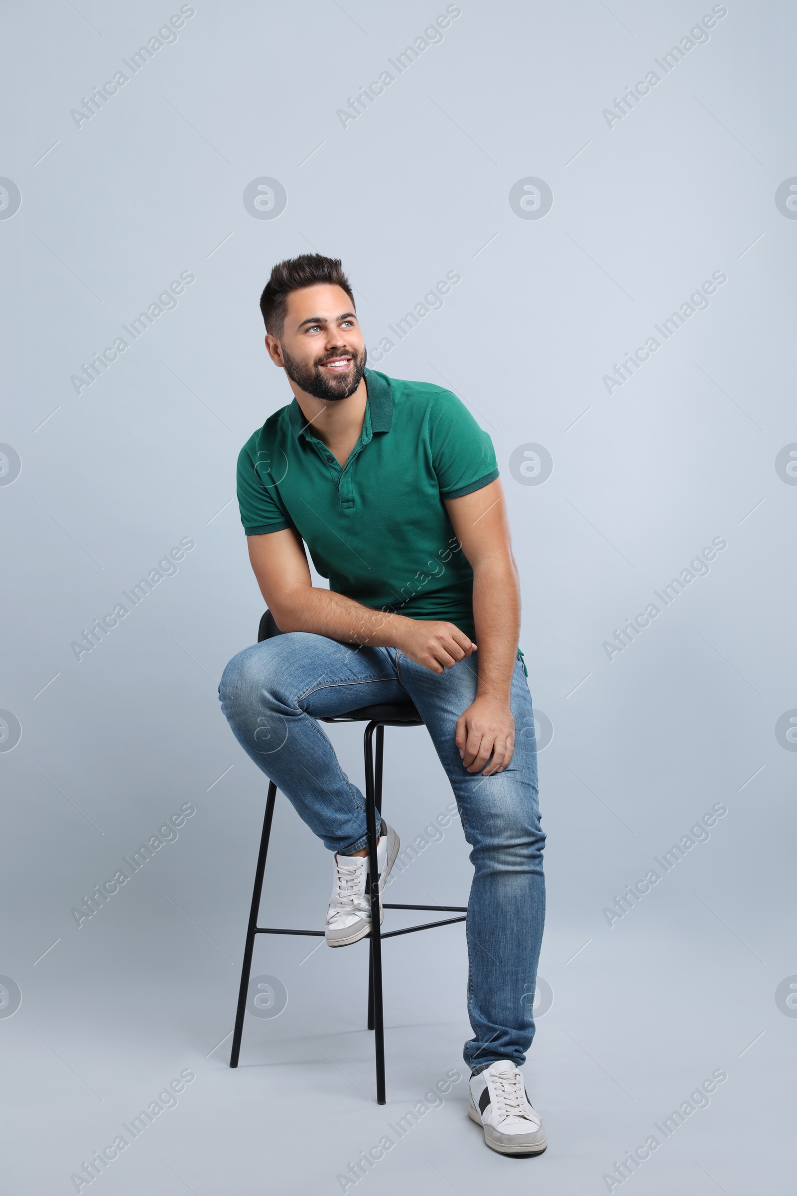 Photo of Handsome young man sitting on stool against light grey background