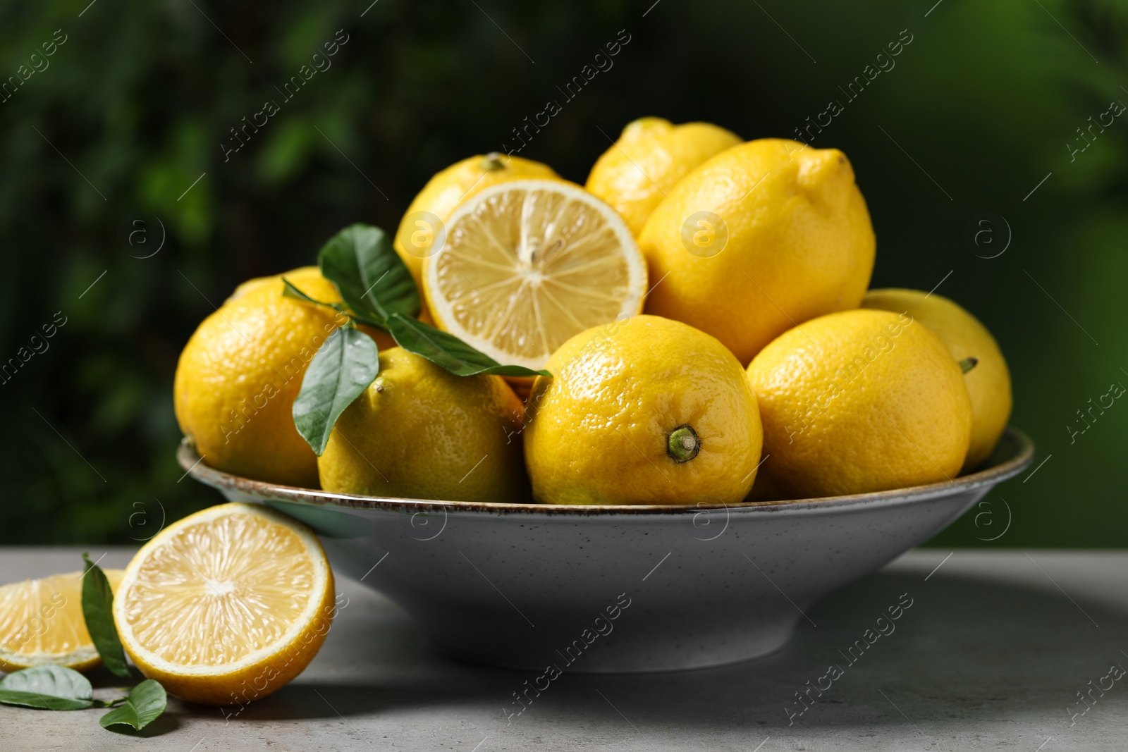 Photo of Fresh lemons and green leaves on grey table outdoors, closeup