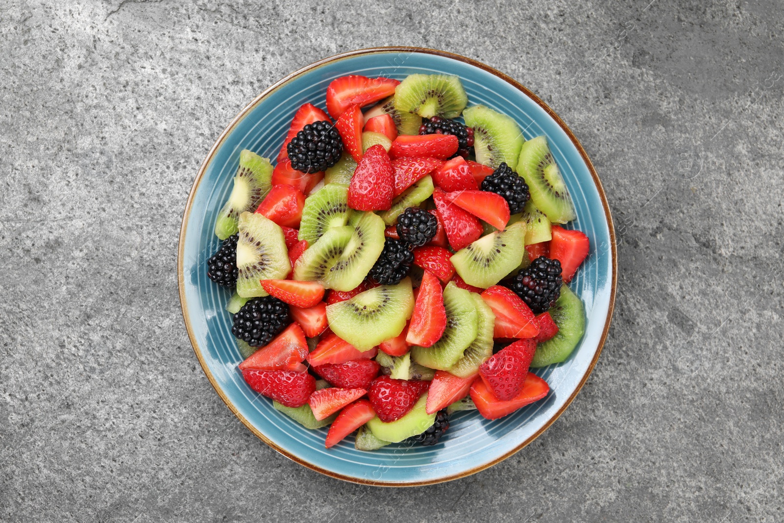 Photo of Plate of delicious fresh fruit salad on grey textured table, top view