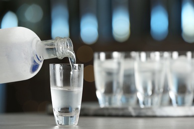 Pouring vodka from bottle into shot glass on bar counter. Space for text