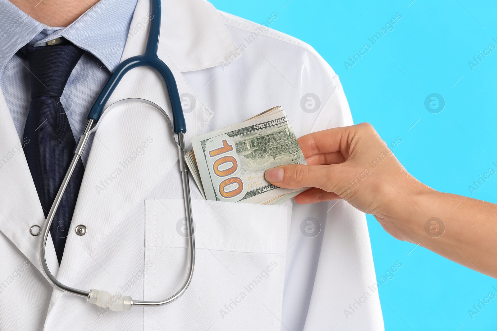 Photo of Patient putting bribe into doctor's pocket on light blue background, closeup. Corruption in medicine