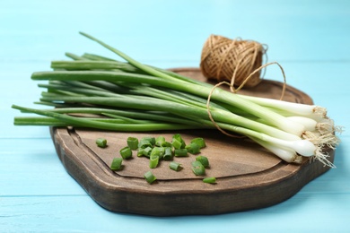 Photo of Wooden board with fresh green onions on light blue table