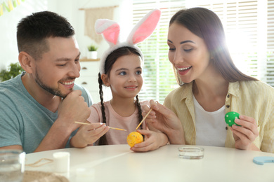 Photo of Happy father, mother and daughter painting Easter eggs at table indoors