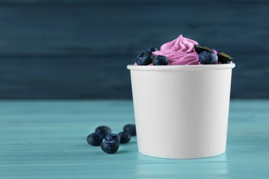 Cup with tasty frozen yogurt and blueberries on blue wooden table. Space for text