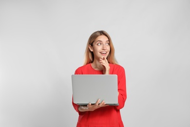 Portrait of emotional woman with modern laptop on light grey background