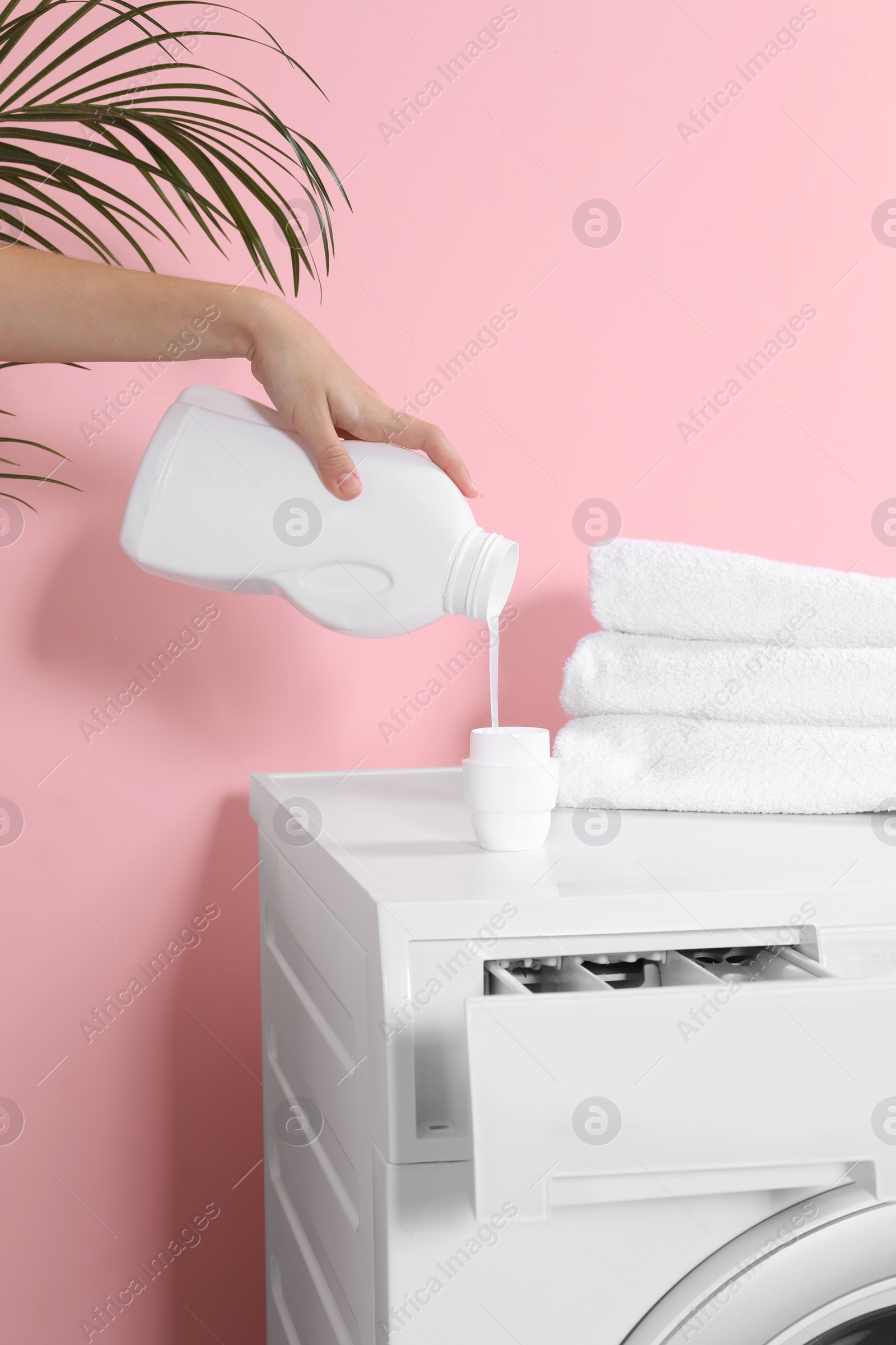 Photo of Woman pouring liquid detergent into cap on washing machine in laundry room, closeup