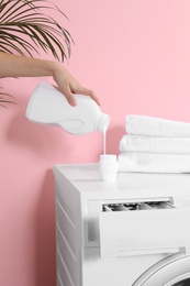 Woman pouring liquid detergent into cap on washing machine in laundry room, closeup