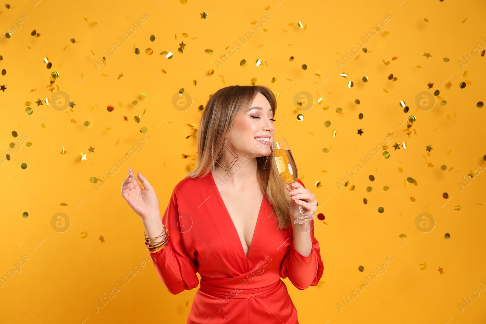 Photo of Happy young woman with glass of champagne and confetti on yellow background