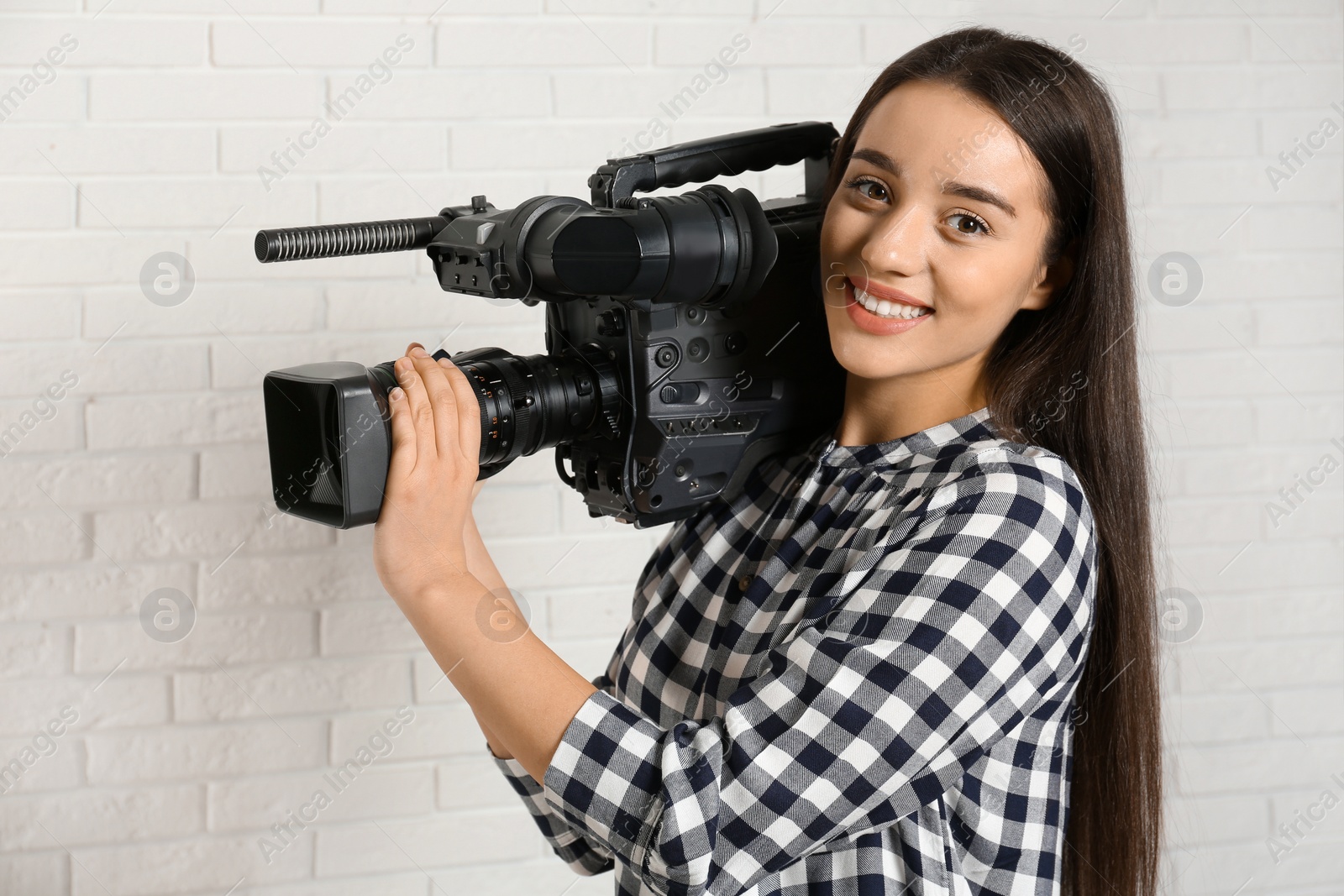 Photo of Operator with professional video camera near white brick wall