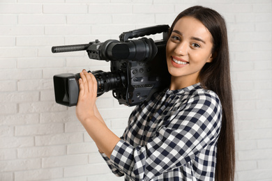 Photo of Operator with professional video camera near white brick wall