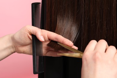 Photo of Hairdresser cutting client's hair with scissors on pink background, closeup
