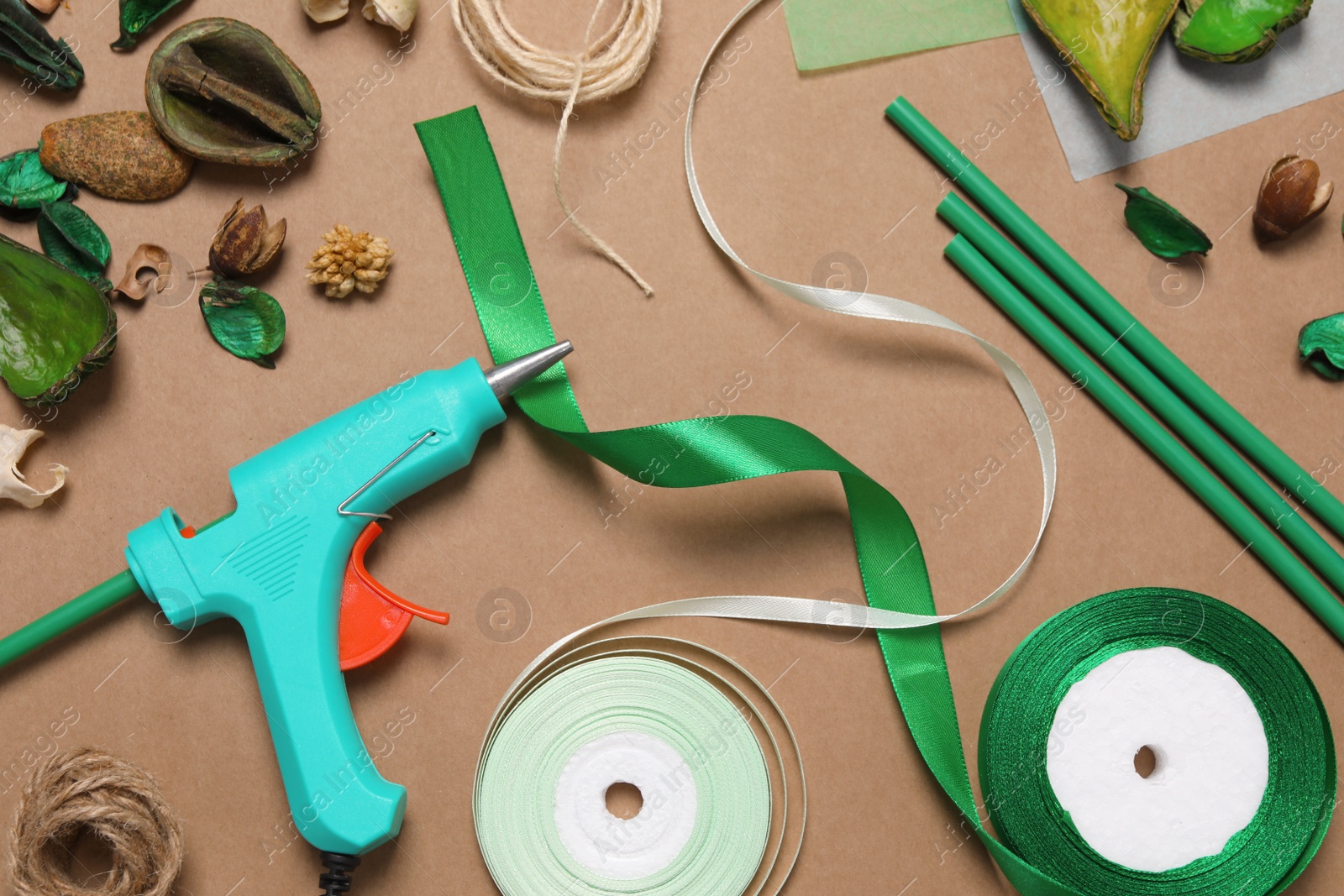 Photo of Hot glue gun and handicraft materials on brown background, flat lay