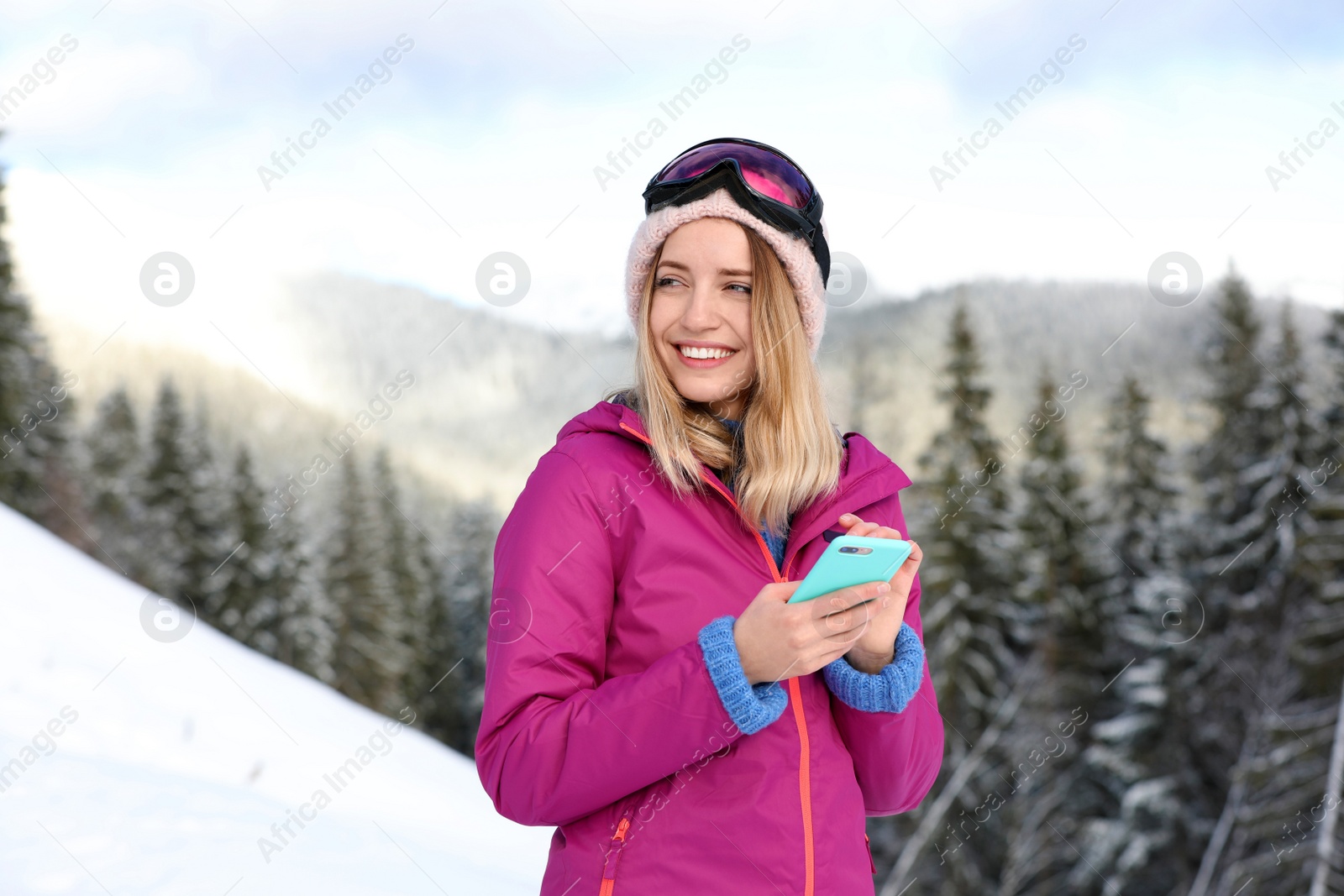 Photo of Young woman with ski goggles using smartphone in mountains during winter vacation
