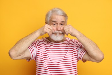 Senior man touching mustache on orange background