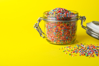 Photo of Colorful sprinkles in jar on yellow background, space for text. Confectionery decor
