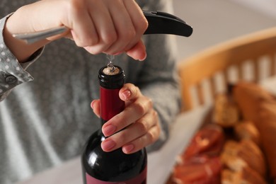 Photo of Woman opening wine bottle with corkscrew at table indoors, closeup