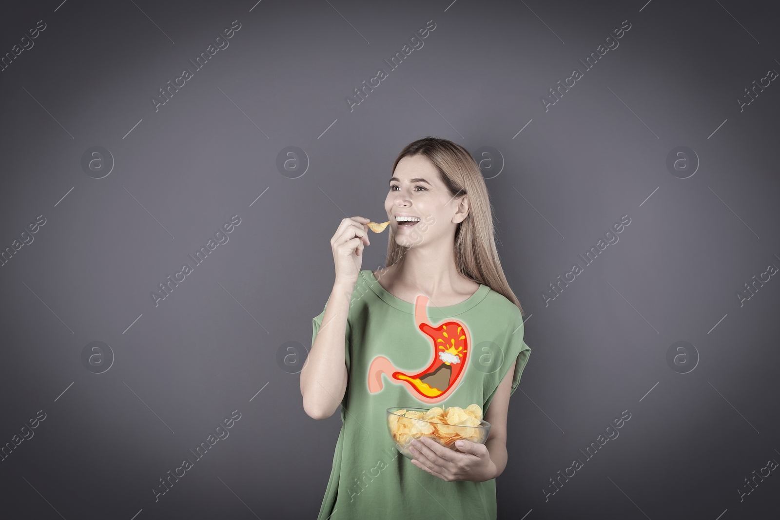 Image of Improper nutrition can lead to heartburn or other gastrointestinal problems. Woman eating potato chips on dark grey background. Illustration of stomach with erupting volcano as acid indigestion