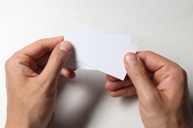 Man holding blank cards at white table, top view. Mockup for design