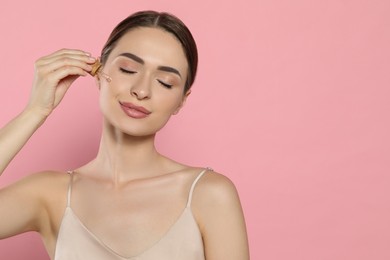 Photo of Young woman applying essential oil onto face on pink background, space for text