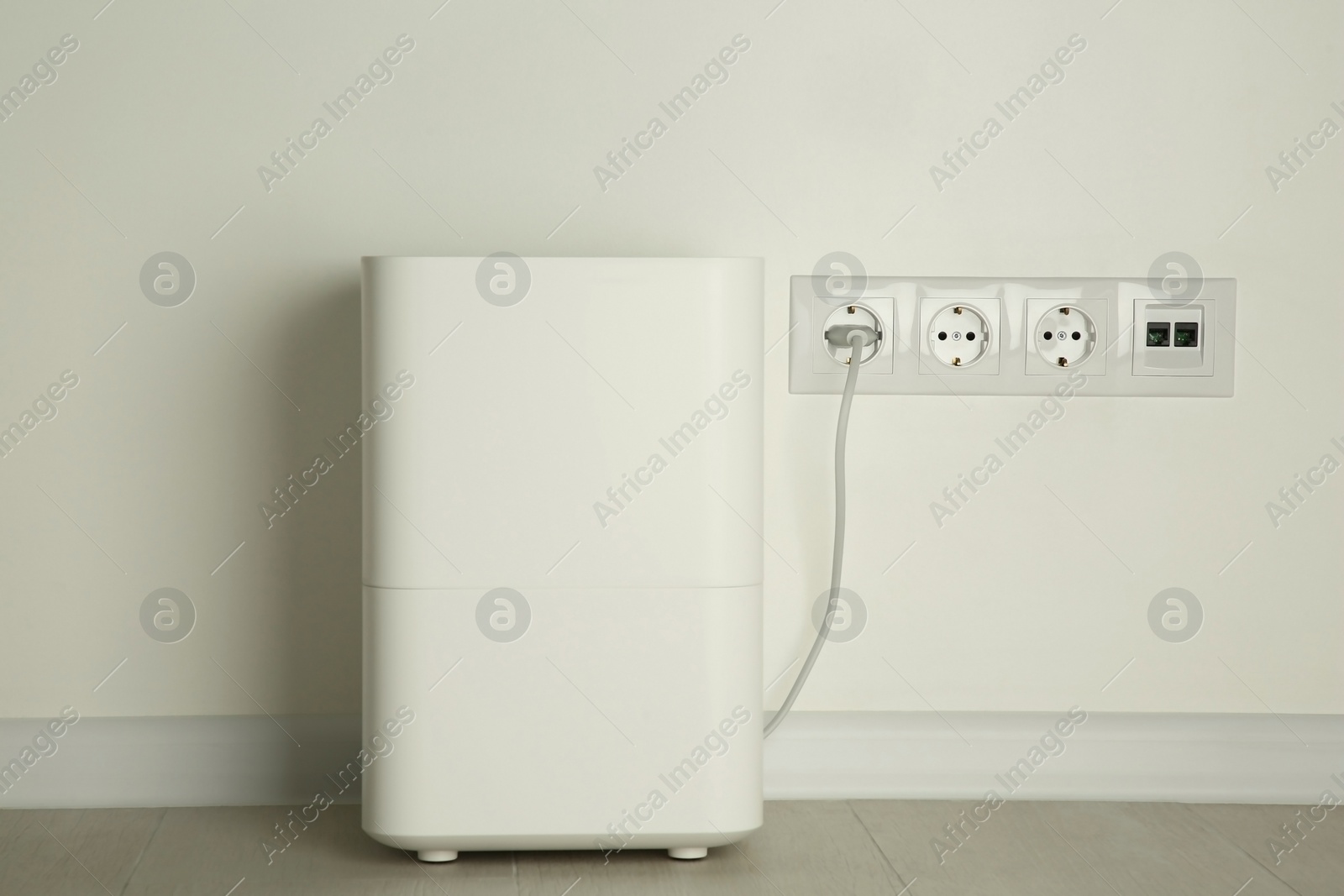 Photo of Modern air humidifier plugged into power socket on floor indoors
