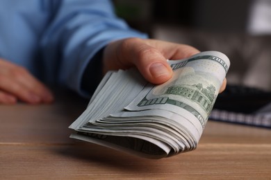 Photo of Money exchange. Woman holding dollar banknotes at wooden table, closeup