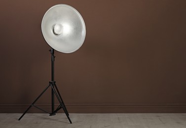 Professional beauty dish reflector on tripod near brown wall in room, space for text. Photography equipment