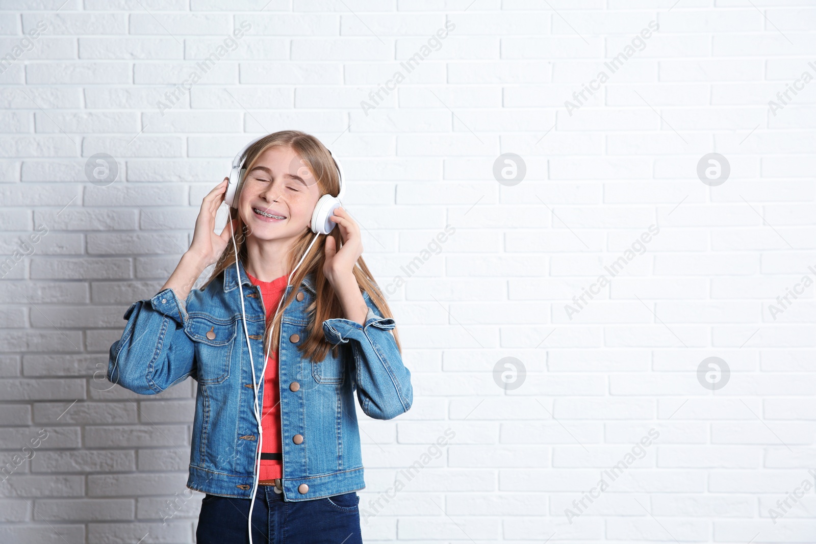 Photo of Teen girl listening to music with headphones near brick wall. Space for text