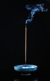 Incense stick smoldering in holder on black background