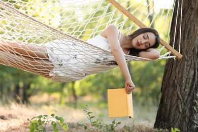 Photo of Young woman with book resting in comfortable hammock at green garden
