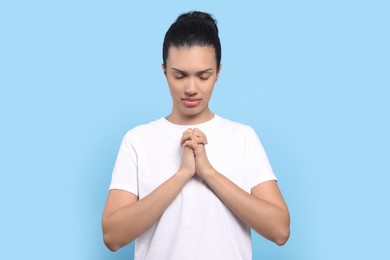 Photo of African American woman with clasped hands praying to God on light blue background