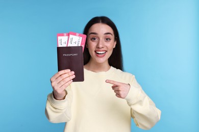 Photo of Happy woman pointing at passport and tickets on light blue background, selective focus