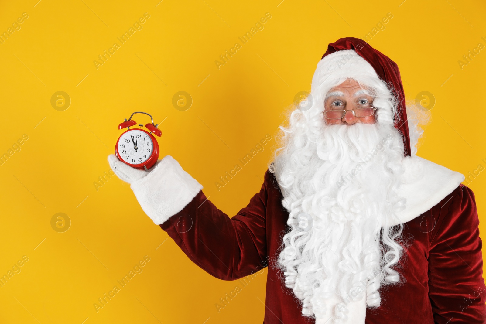 Photo of Santa Claus holding alarm clock on yellow background. Christmas countdown