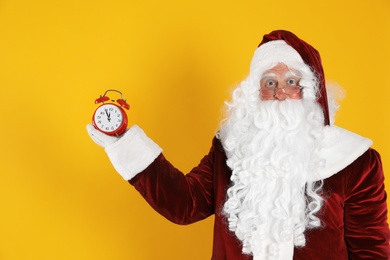 Photo of Santa Claus holding alarm clock on yellow background. Christmas countdown