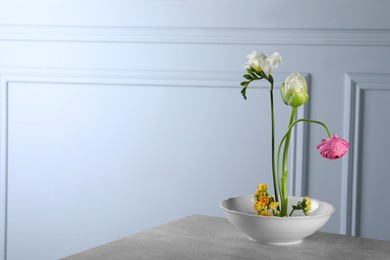 Stylish ikebana as house decor. Beautiful fresh flowers on grey table near white wall, space for text